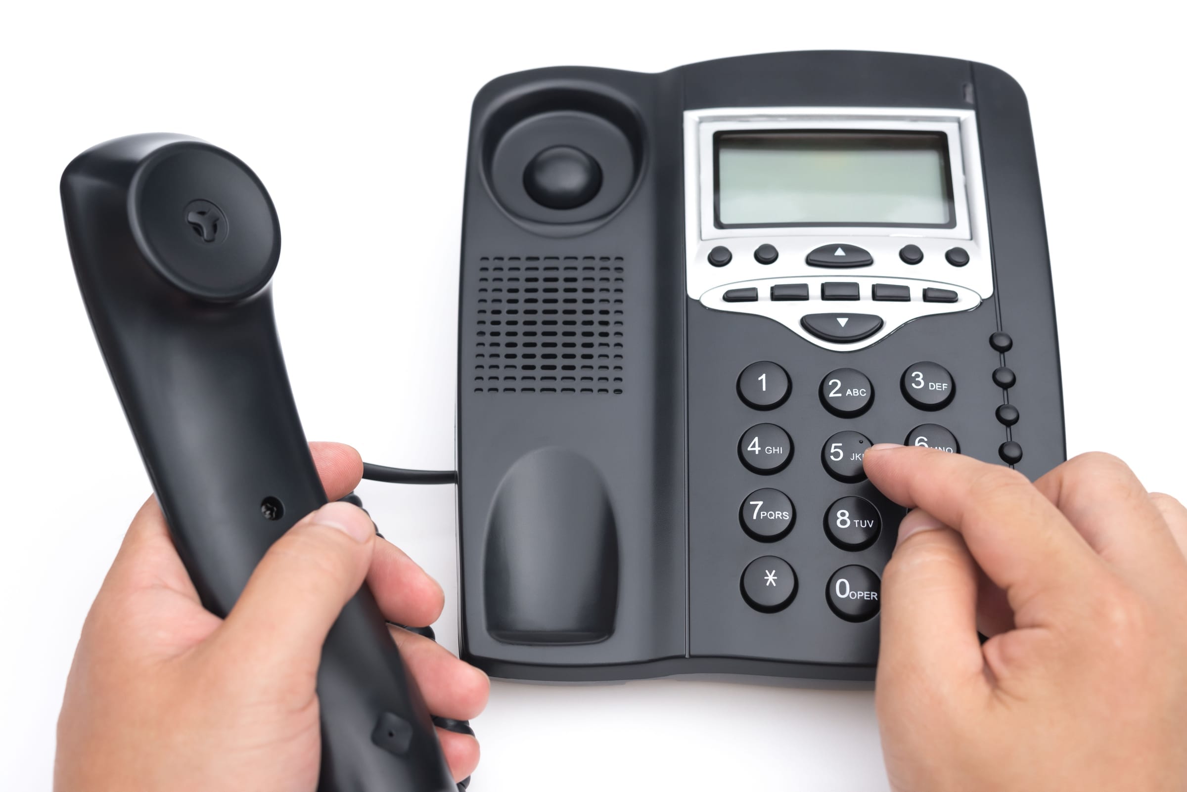 Hands lifting the handset and dialing a desk telephone.